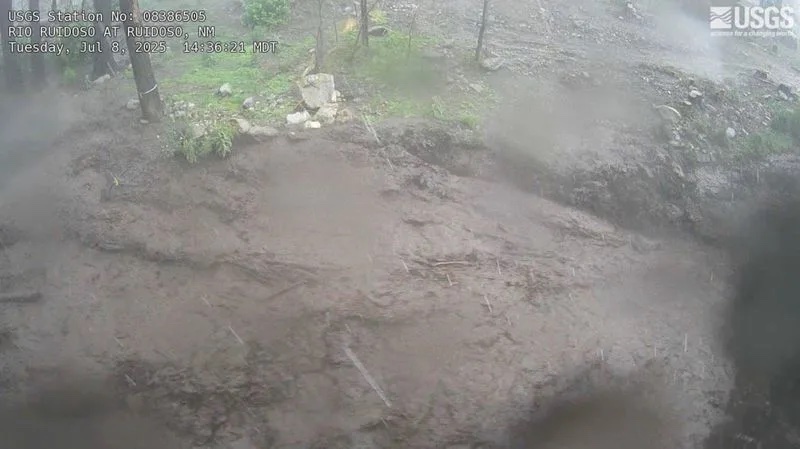 Frame from the USGS flood camera on the Rio Ruidoso at Ruidoso on July 8, 2025 at 2:36 PM, showing the channel running bank to bank with brown floodwater